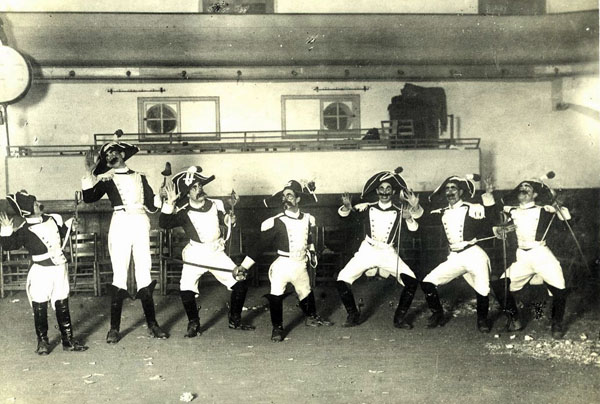 Retrat de la colla de Carnaval dels “Nyinyus” formada pel “Nyinyo”, en Felip, en Salmeron, el Gruixut, en Cosme, en Manau i en Clarel, caracteritzats com a carabinieri per representar el número dels calabresos en el segon ball de la temporada carnavalesca de l’any 1921 al Teatre Vidal. AMSFG. Col·lecció Santiago Güitó (Autor: Desconegut)