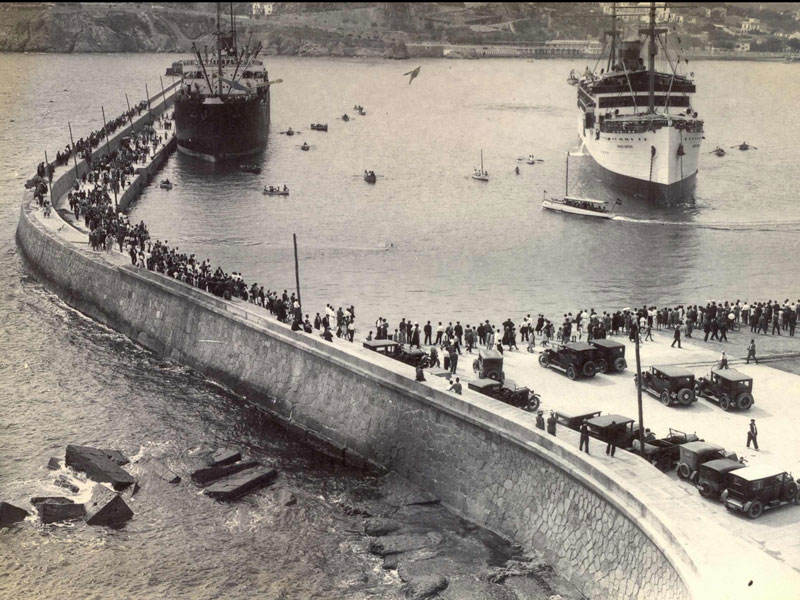 El port comercial de Sant Feliu ple de gent esperant l’arribada d’un vaixell de passatgers (1925 – 1935). AMSFG. Fons Espuña – Ibañez. Autor: Desconegut.