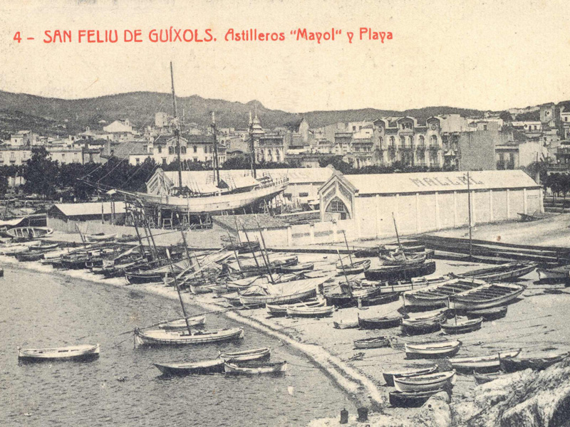 Les drassanes Mallol al racó de Llevant de la platja de Sant Feliu amb el veler Sant Jordi en construcció (1918 – 1921). AMSFG. Fons Ajuntament de Sant Feliu de Guíxols. Autor: Desconegut.