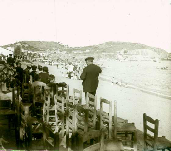 Platja de Sant Feliu de Guíxols amb ambient de festa i els llaguts adornats amb banderes espanyoles, 1919. AMSFG. Fons Francesc Llorens (Autor: Francesc Llorens)